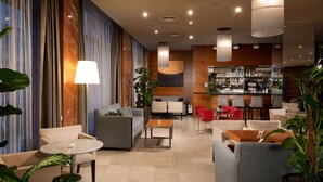 Un hall d’hôtel moderne doté d’un bar, de coins salon et d’une grande plante.