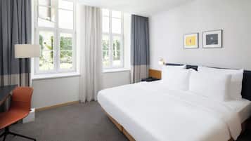 A hotel room with a bed, a desk, a chair, and a window with curtains.