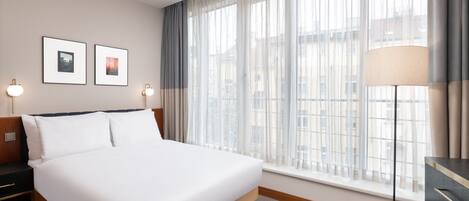 A hotel room with a large bed, a nightstand, a lamp, and a window with curtains.