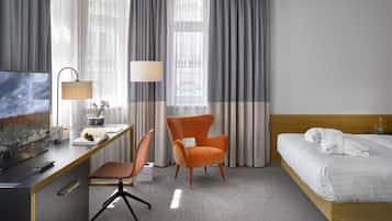 Habitación de hotel con cama, escritorio, silla, televisor y lámpara.