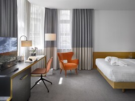 Een hotelkamer met een bed, een bureau met stoel, een televisie en een lamp.