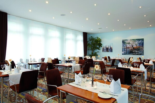 A hotel dining area with multiple tables set for dining, chairs, and a large window with curtains. - Seaside Residenz Hotel Chemnitz (Chemnitz)