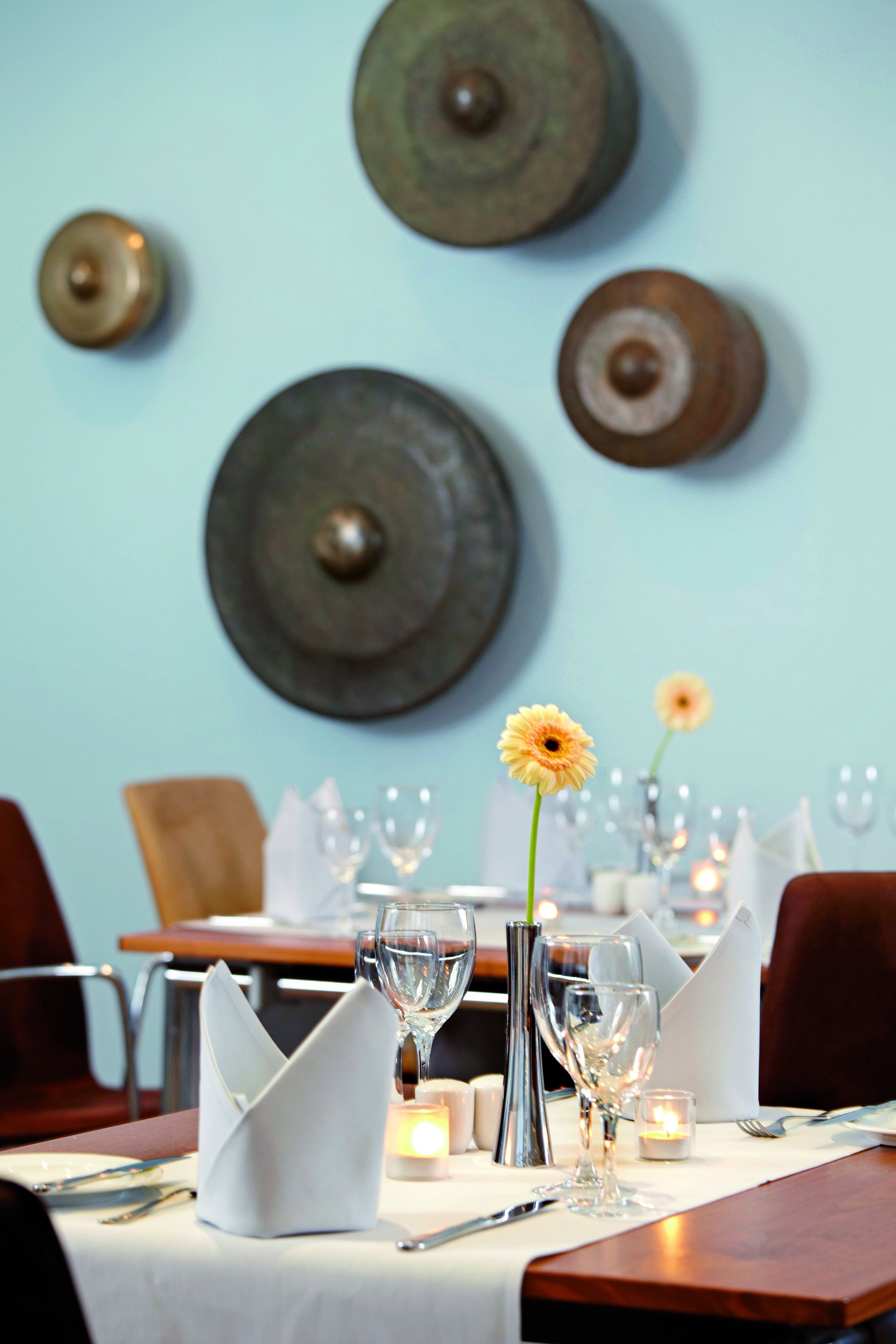 A dining table set with white napkins, silverware, and wine glasses, with a candle and a vase with a single flower on the table.