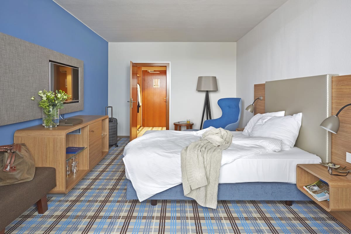 A hotel room with a bed, bedside table, lamp, chair, desk, and a mirror.