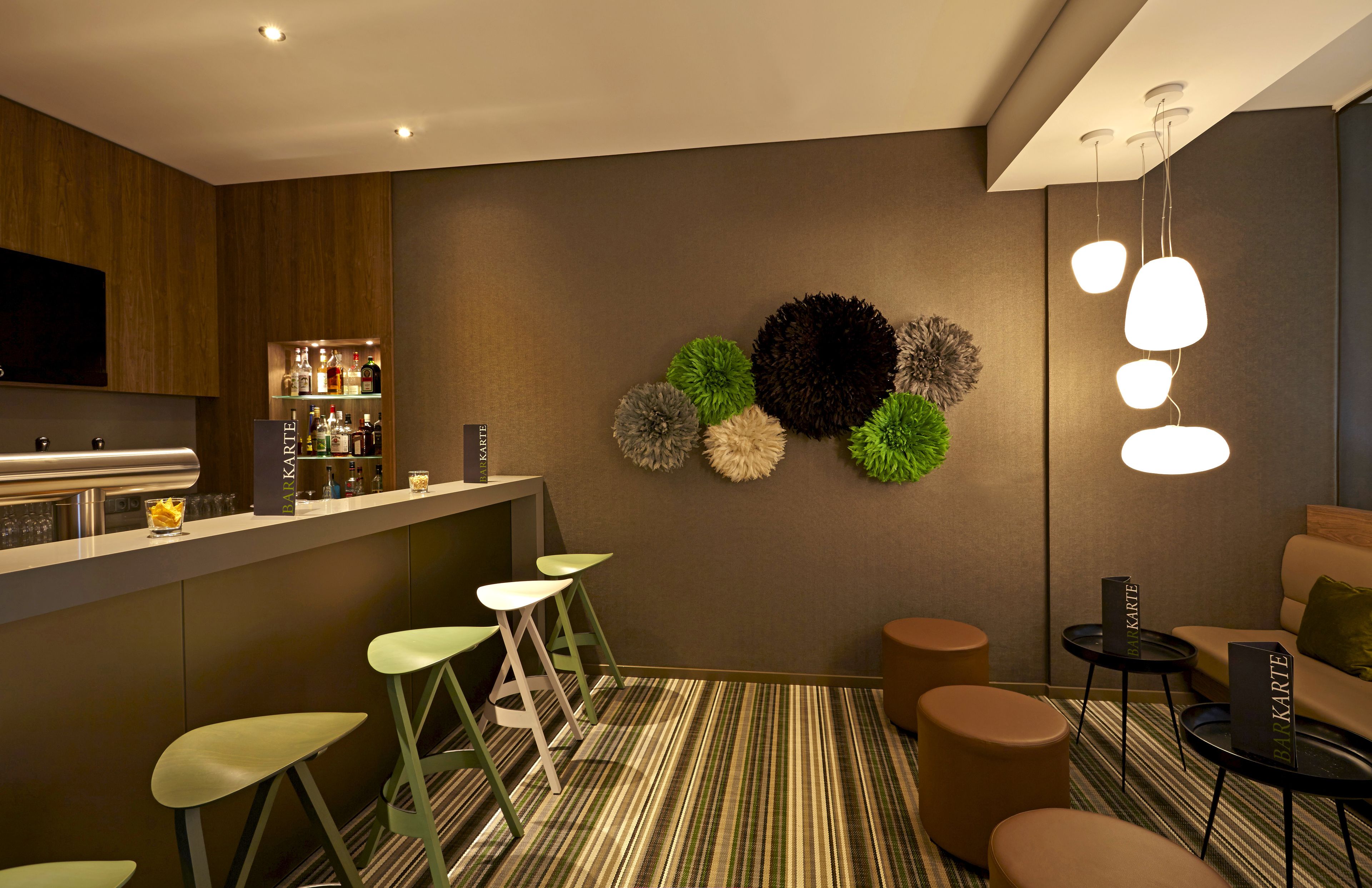 A modern kitchen with a bar area, green bar stools, and a seating area with a sofa and ottoman.