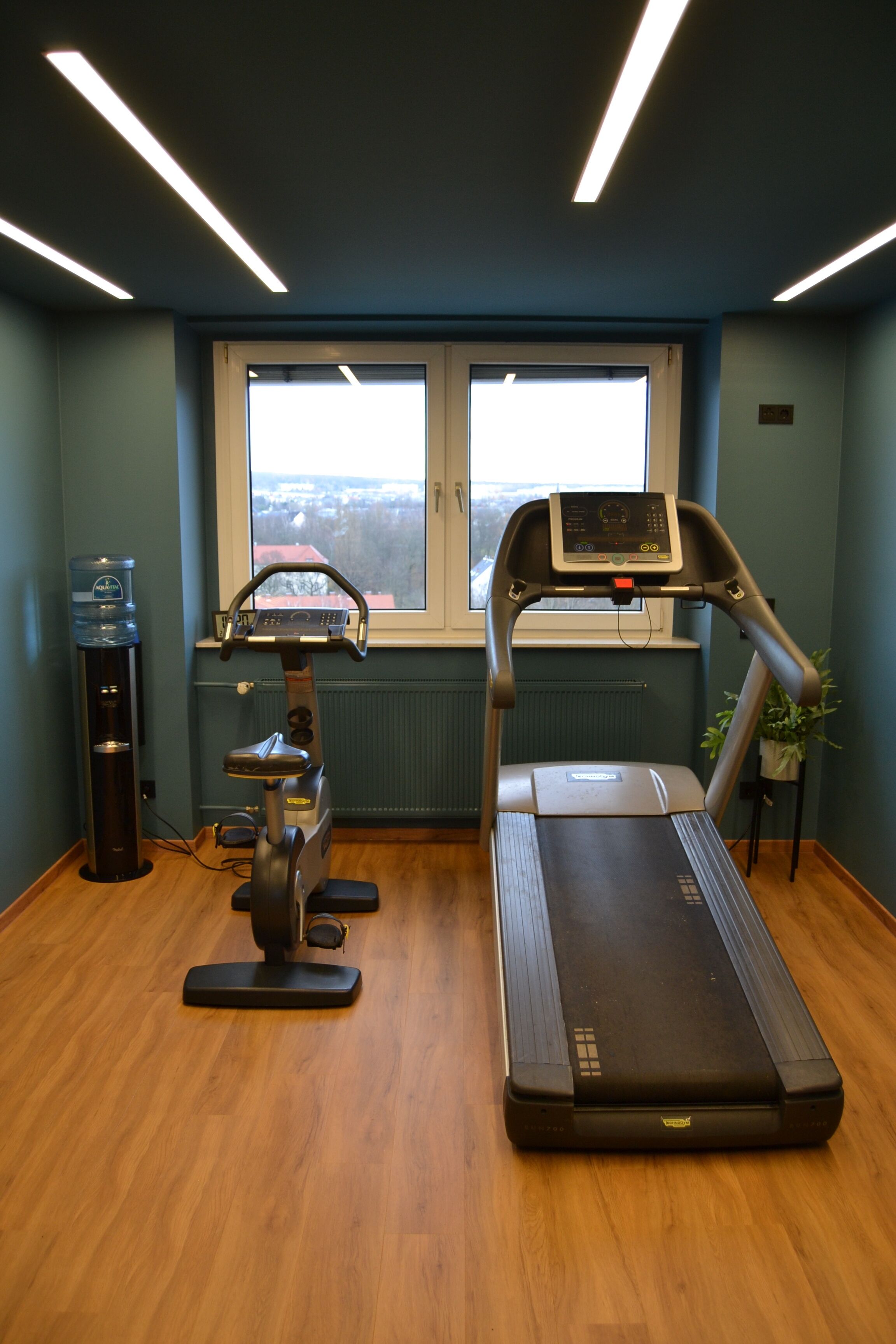 Ein Fitnessraum mit Laufband, Wasserspender und Ergometer.
