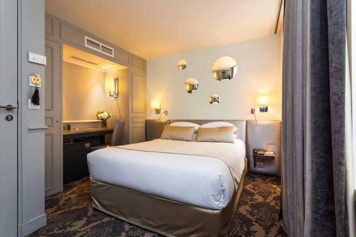 A hotel room with a large bed, bedside tables, a desk, and a mirror.
