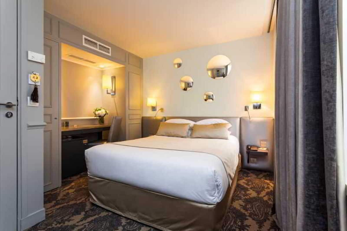 Una habitación de hotel con una cama grande, mesitas de noche, un escritorio y un espejo.