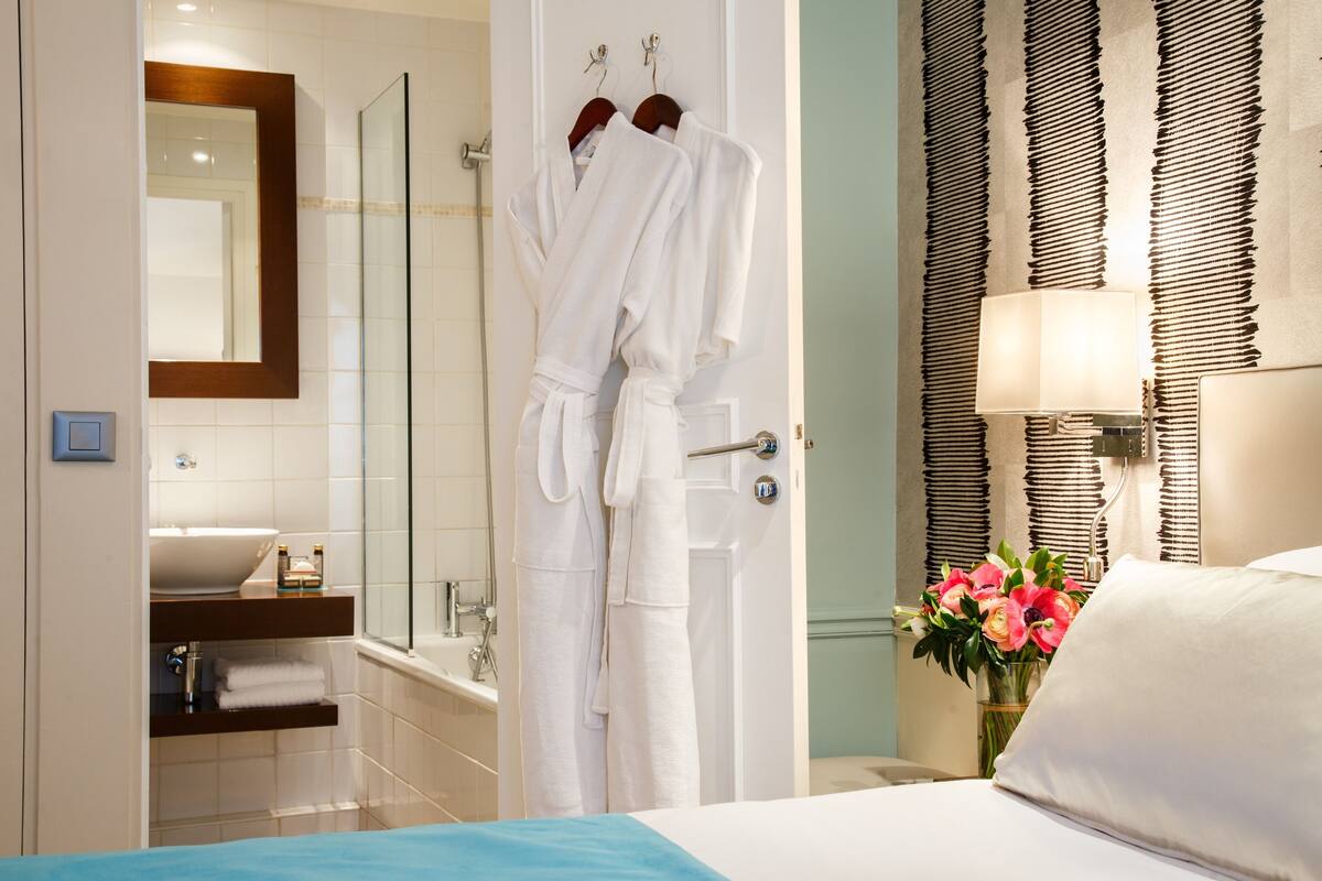 A hotel bathroom with a glass shower, a sink, and a mirror. There are two white robes hanging on a rack.