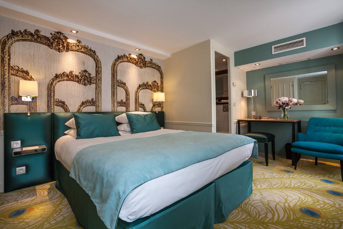 A hotel room with a large bed, a desk, and a chair. There are two lamps on the nightstands.