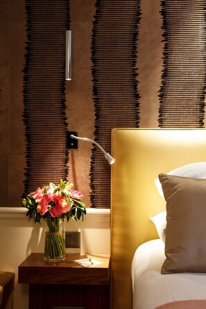 A hotel room with a bed, a nightstand with a vase of flowers, and a wall-mounted light fixture. - Hotel Le Clos Medicis (Paris)
