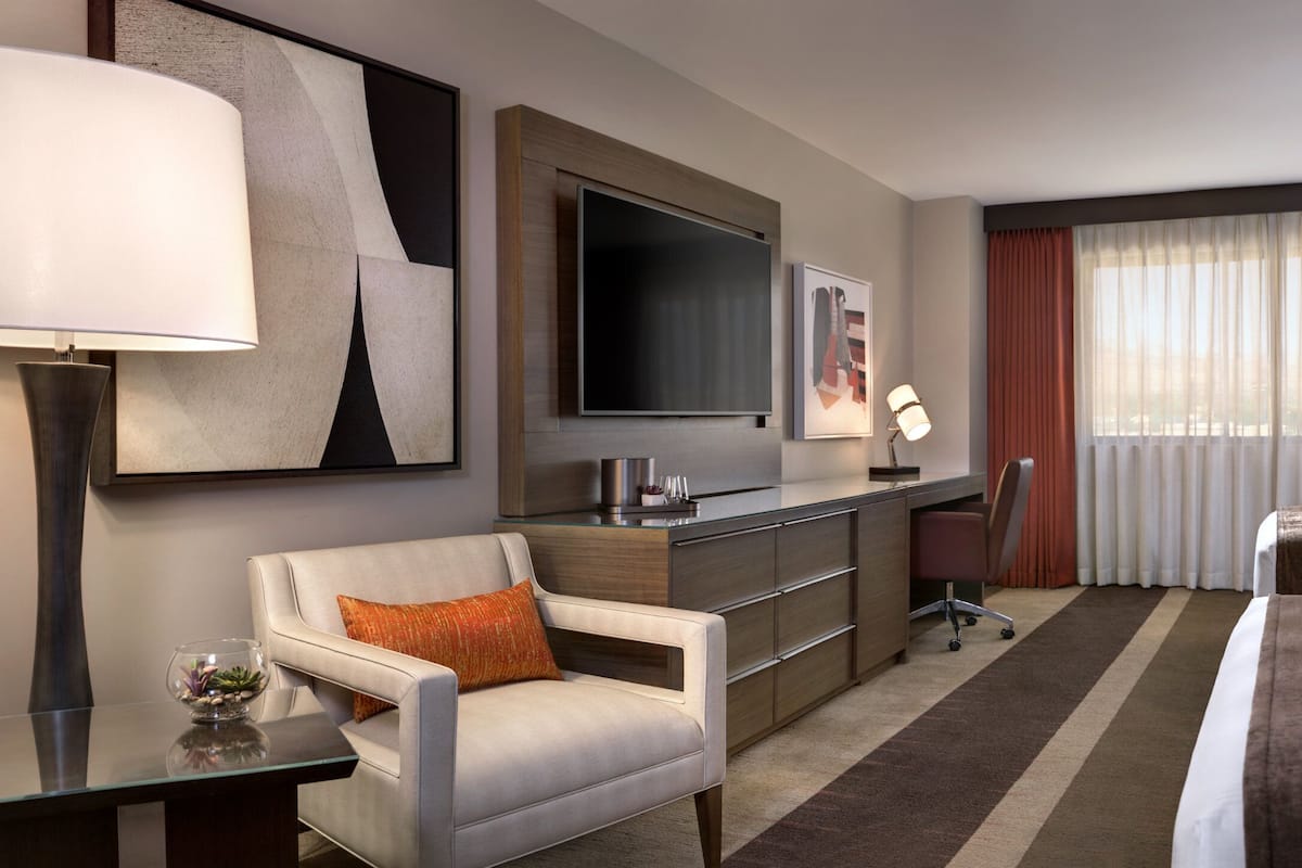 A hotel room with a bed, a desk, a chair, a TV, and a window with curtains.