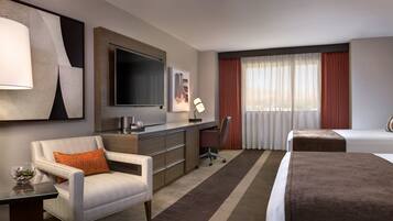 A hotel room with a bed, a desk, a chair, a TV, and a window with curtains.