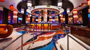 Zona de bar moderna con barra circular, diversas opciones de asientos y un llamativo diseño de suelo con colores vivos.