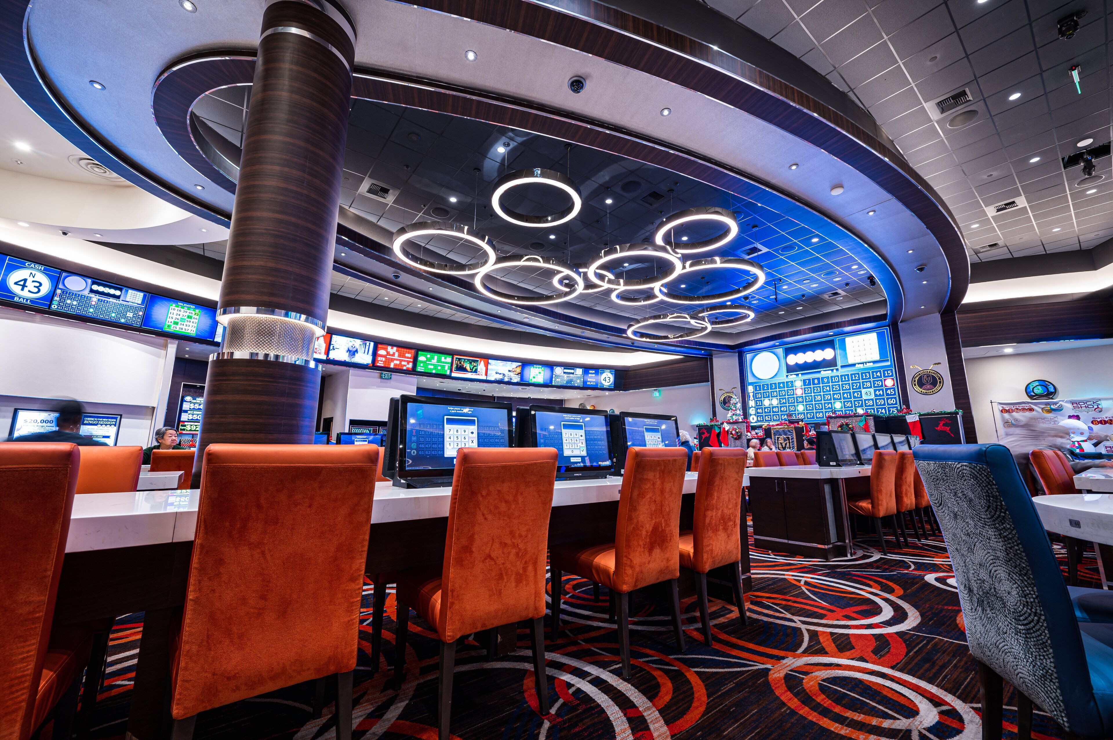 A modern hotel lobby with a central column, multiple monitors, and orange seating.
