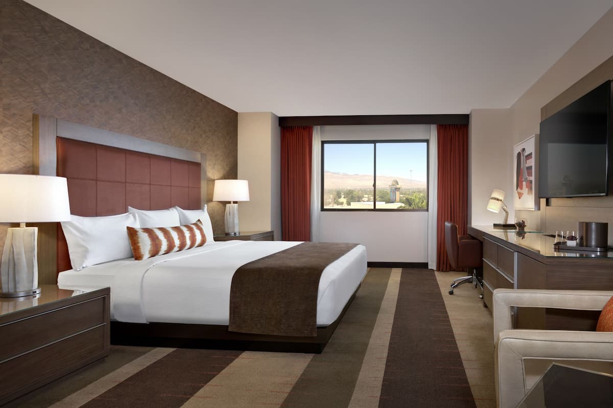 A hotel room with a bed, a desk, a chair, a TV, and a window with a view of the mountains.