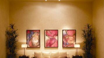 A lobby with a large chandelier, three abstract paintings, two potted plants, a sofa, and a tiled floor.