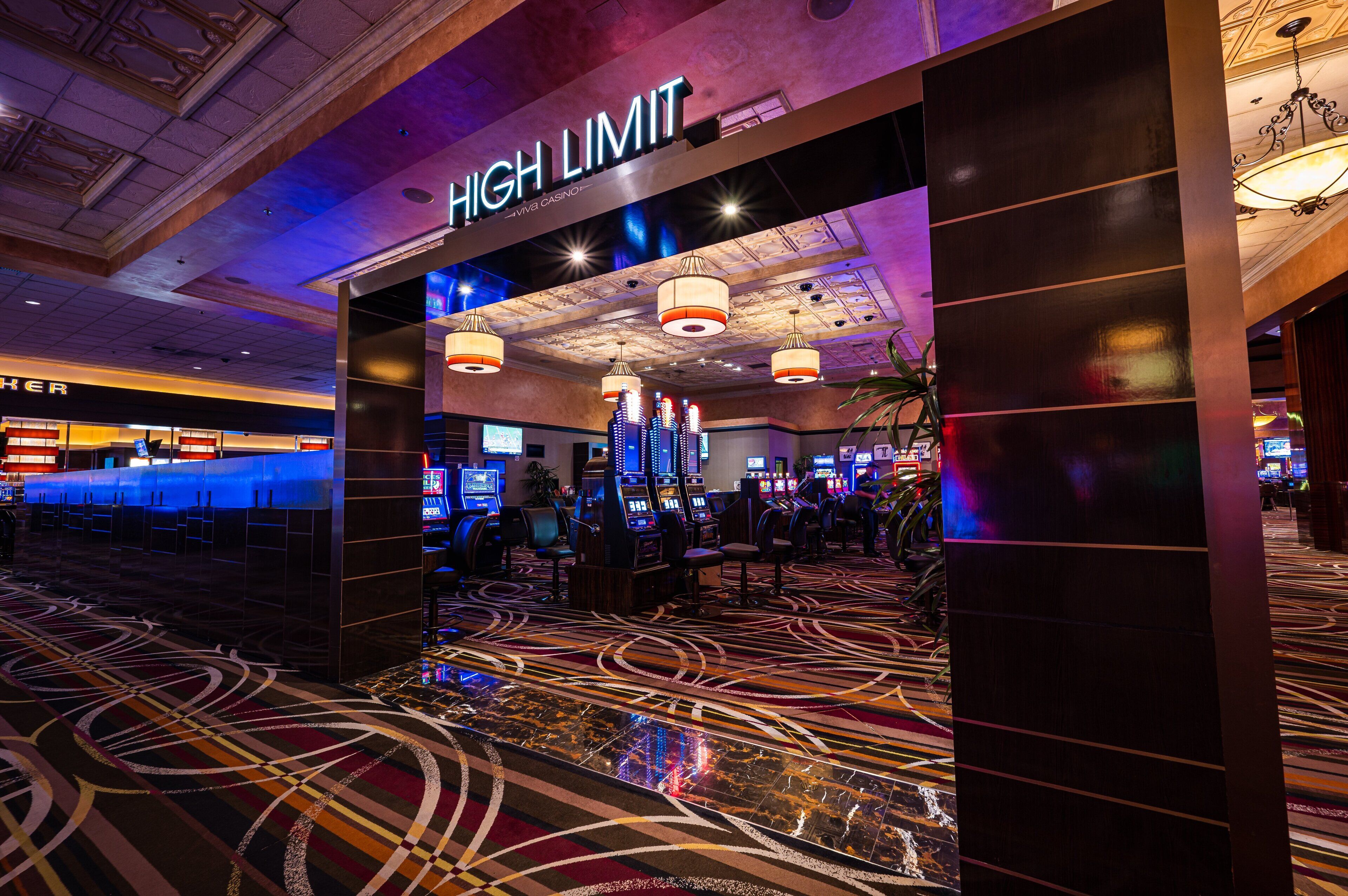 Ein Casino-Innenraum mit einem 'High Limit'-Schild, Spielautomaten und einem gemusterten Teppich.