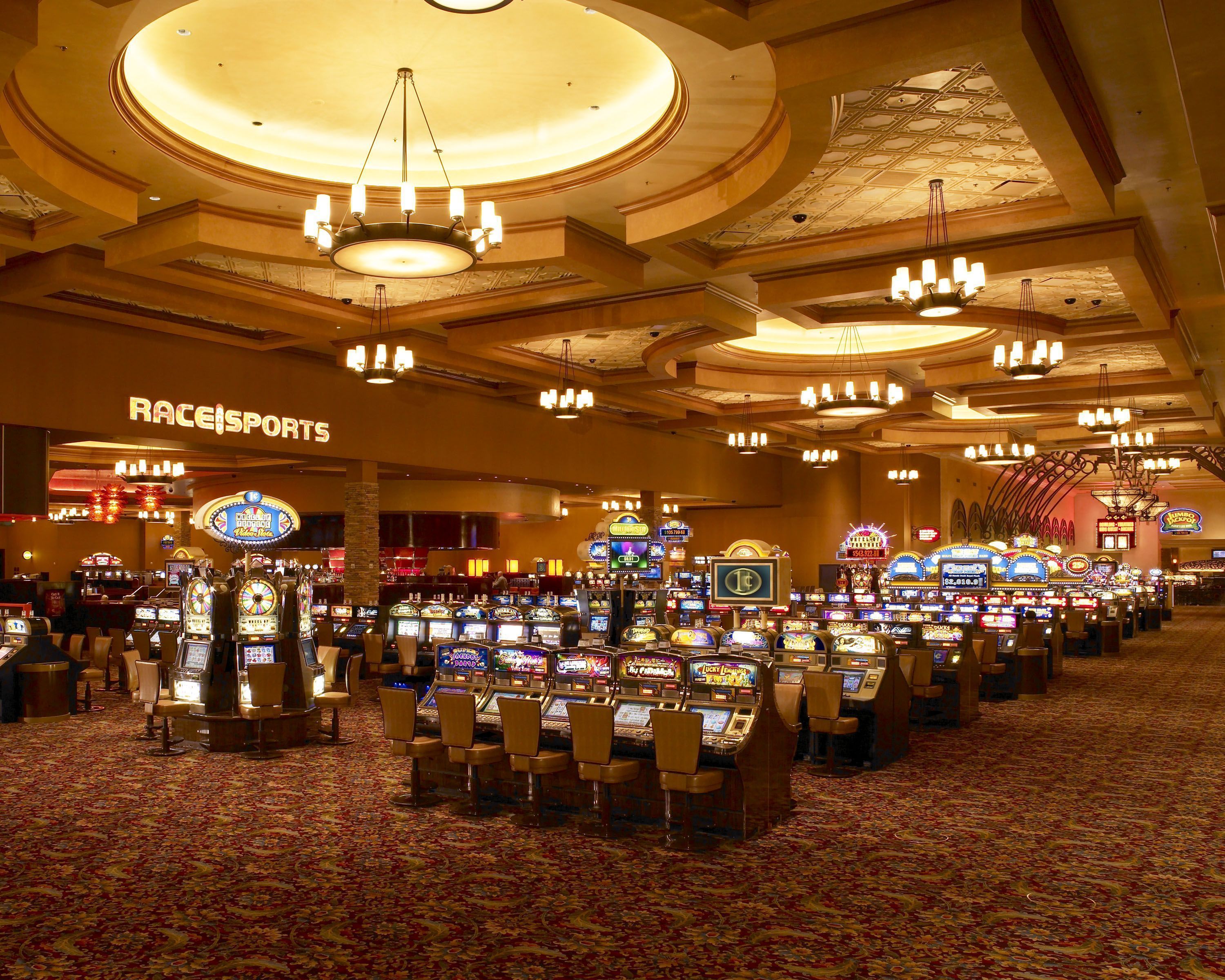 Un casino con múltiples máquinas tragamonedas y un letrero que dice 'RaceSports'.
