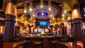 Zona de bar con diversas opciones de asientos, una barra central e iluminación decorativa en el techo.