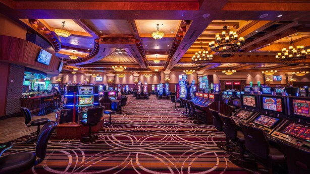 Un casino amb diverses taules de joc i màquines escurabutxaques, una zona de bar i una catifa amb disseny.