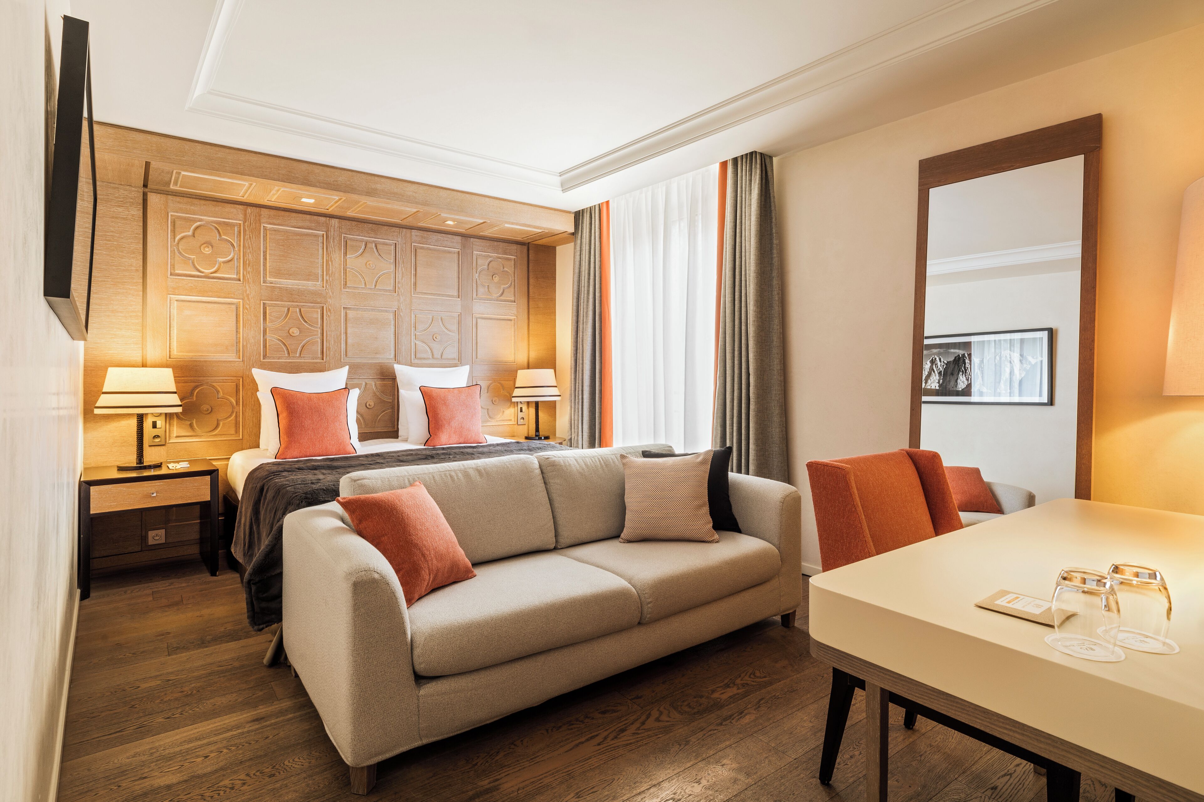 Una habitación de hotel con cama, sofá, mesa de comedor y cabecero de madera.