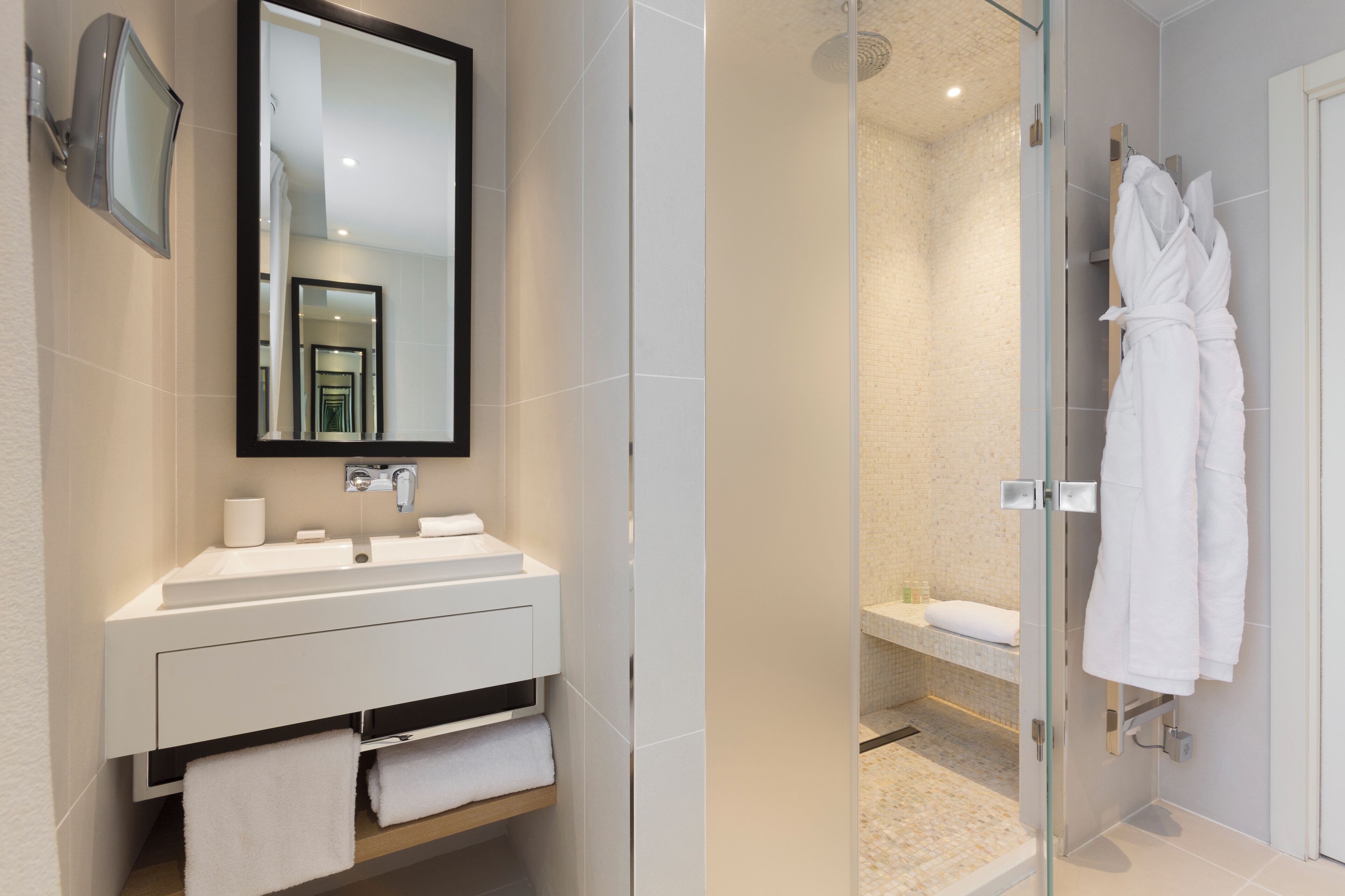 A modern bathroom with a large mirror, white sink, and glass-enclosed shower.
