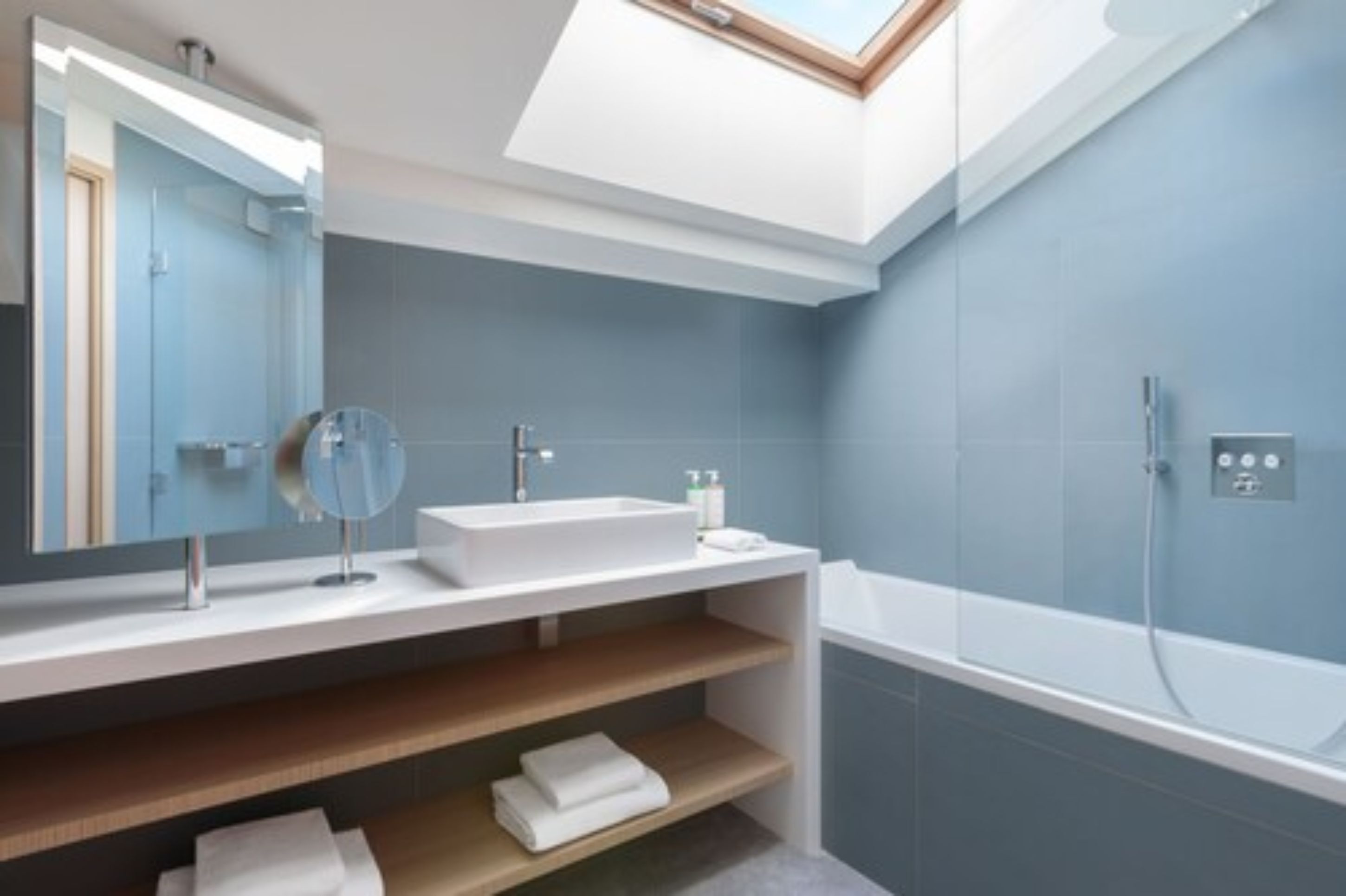 Une salle de bain moderne dotée d’une lucarne, d’une baignoire sur pieds et d’un meuble-lavabo avec un miroir et un évier.