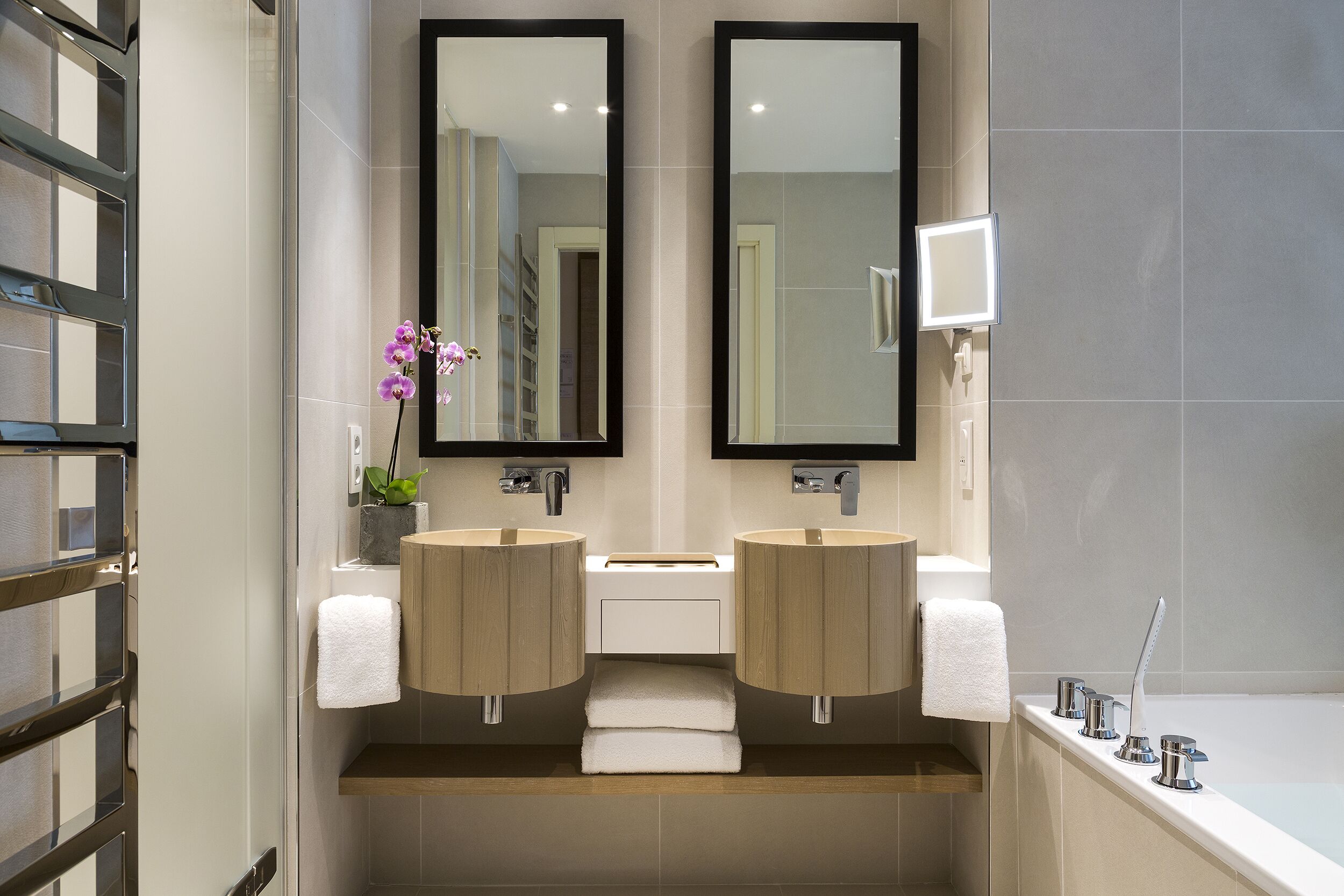 Un baño moderno con dos lavamanos, un espejo, un perchero para toallas y una zona de ducha.