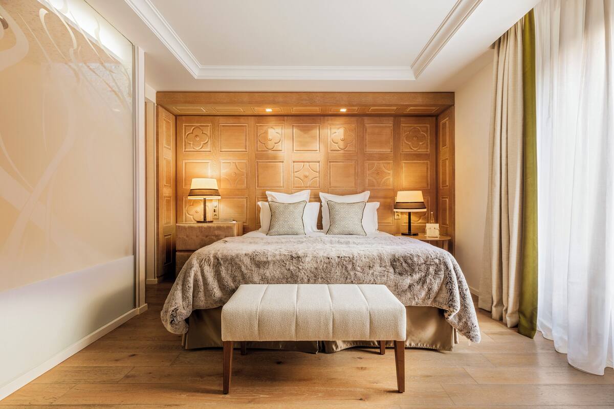 Une chambre à coucher avec un grand lit, deux tables de chevet, un banc et une tête de lit en bois.