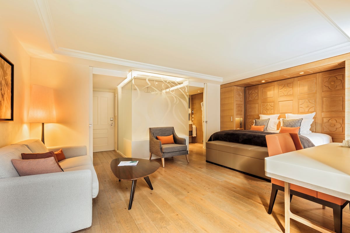 Une chambre d’hôtel avec un lit, un canapé, une chaise, une table et un plancher en bois.