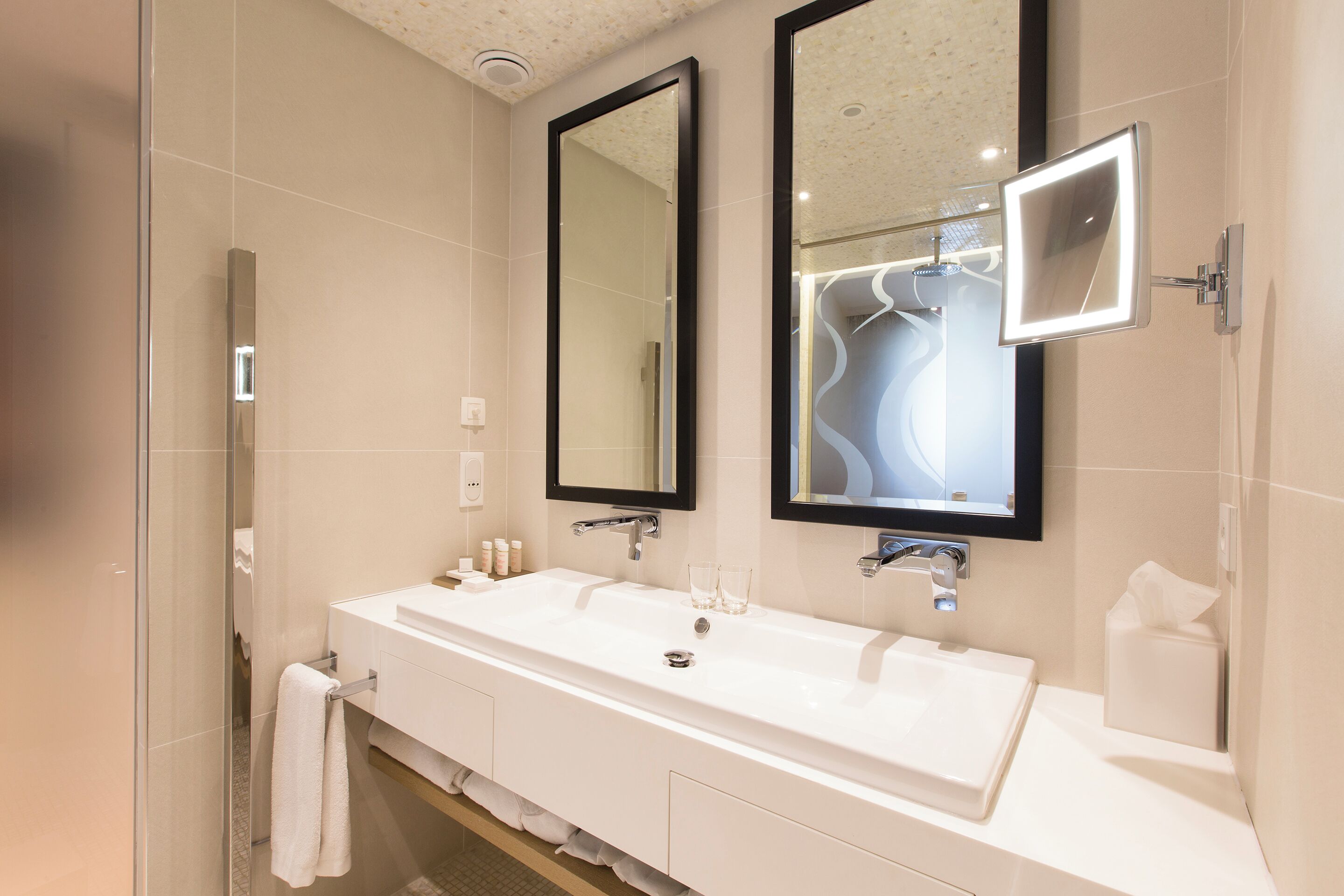 Un baño moderno con un lavamanos grande de color blanco, dos espejos y una cabina de ducha de vidrio.