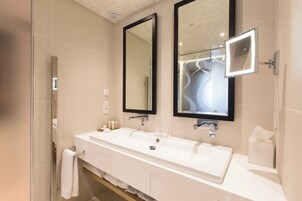 Un baño moderno con un lavamanos grande de color blanco, dos espejos y una cabina de ducha de vidrio.