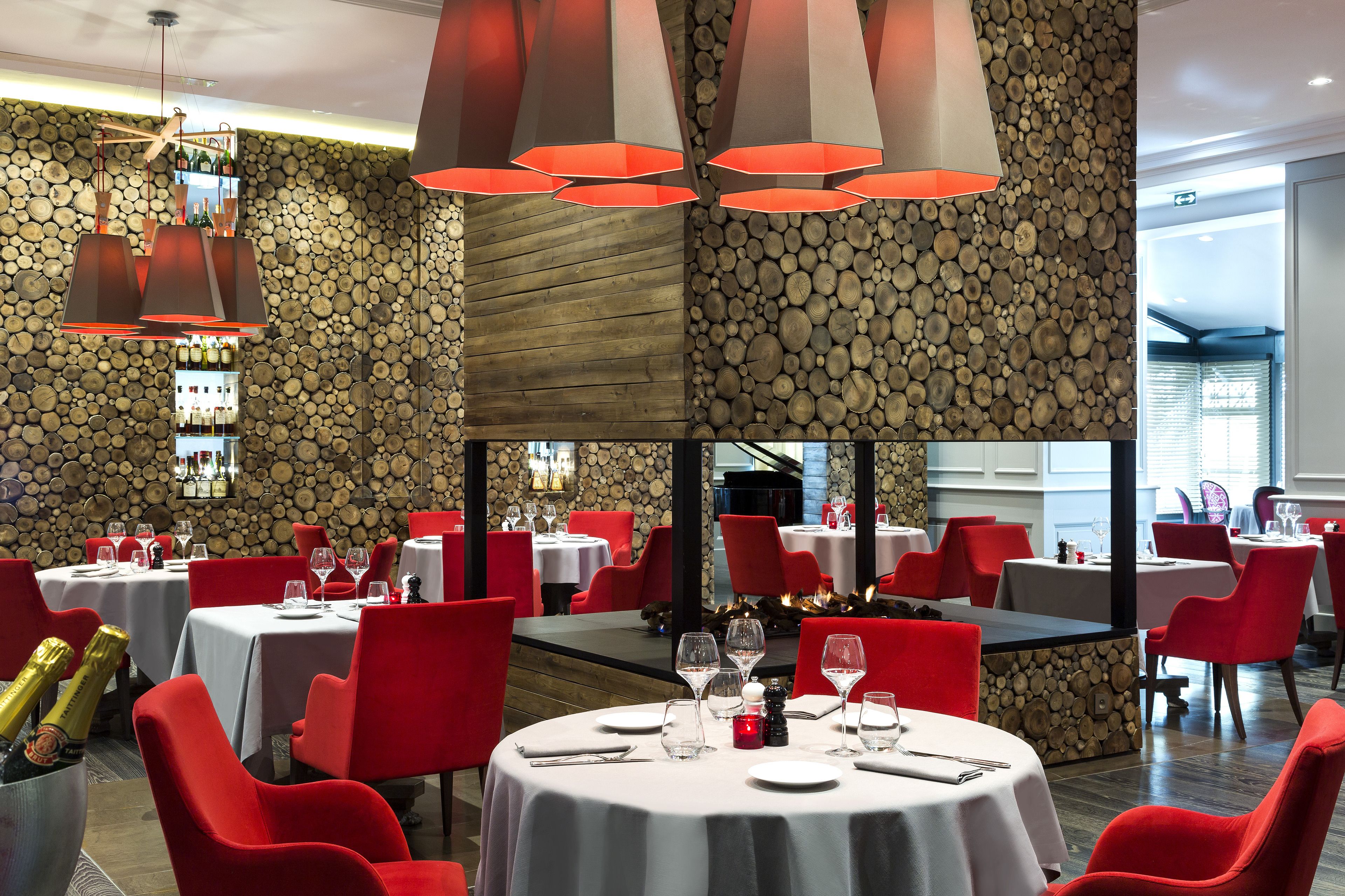 Un restaurant avec des tables rondes, des chaises rouges et un mur en pierre.