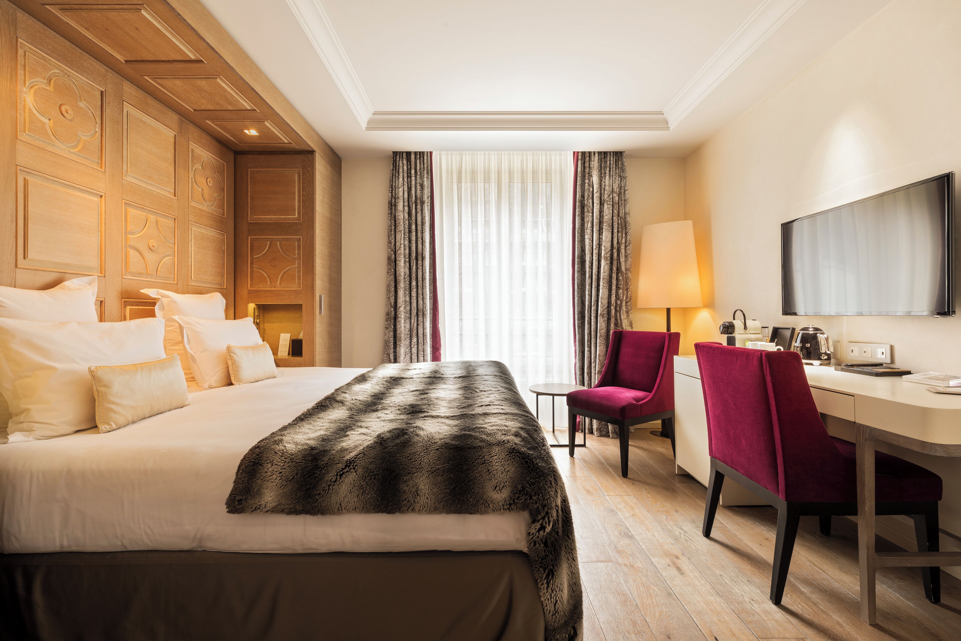Hotelkamer met een groot bed, een bureau, een stoel, een televisie en een raam met gordijnen.