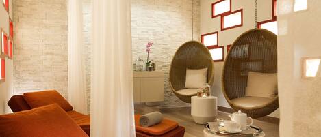A modern spa room with a stone wall, orange seating, wicker chairs, and a white coffee table with a tray.