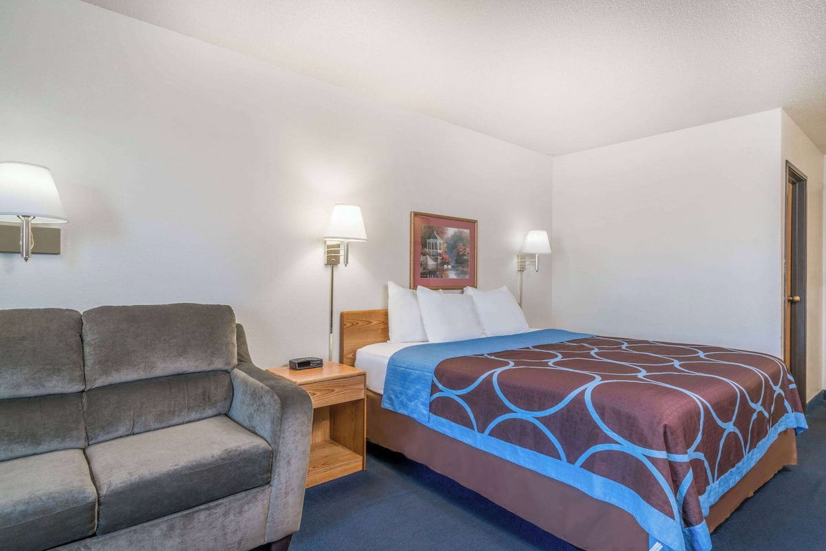 A hotel room with a bed, a sofa, two bedside lamps, a nightstand, and a framed picture on the wall.