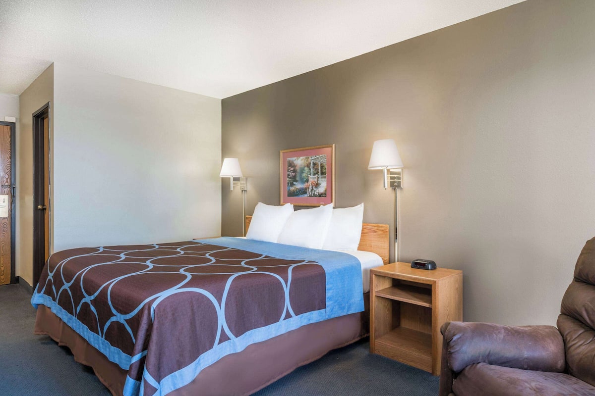 A hotel room with a bed, two bedside lamps, a nightstand, a chair, and a painting on the wall.
