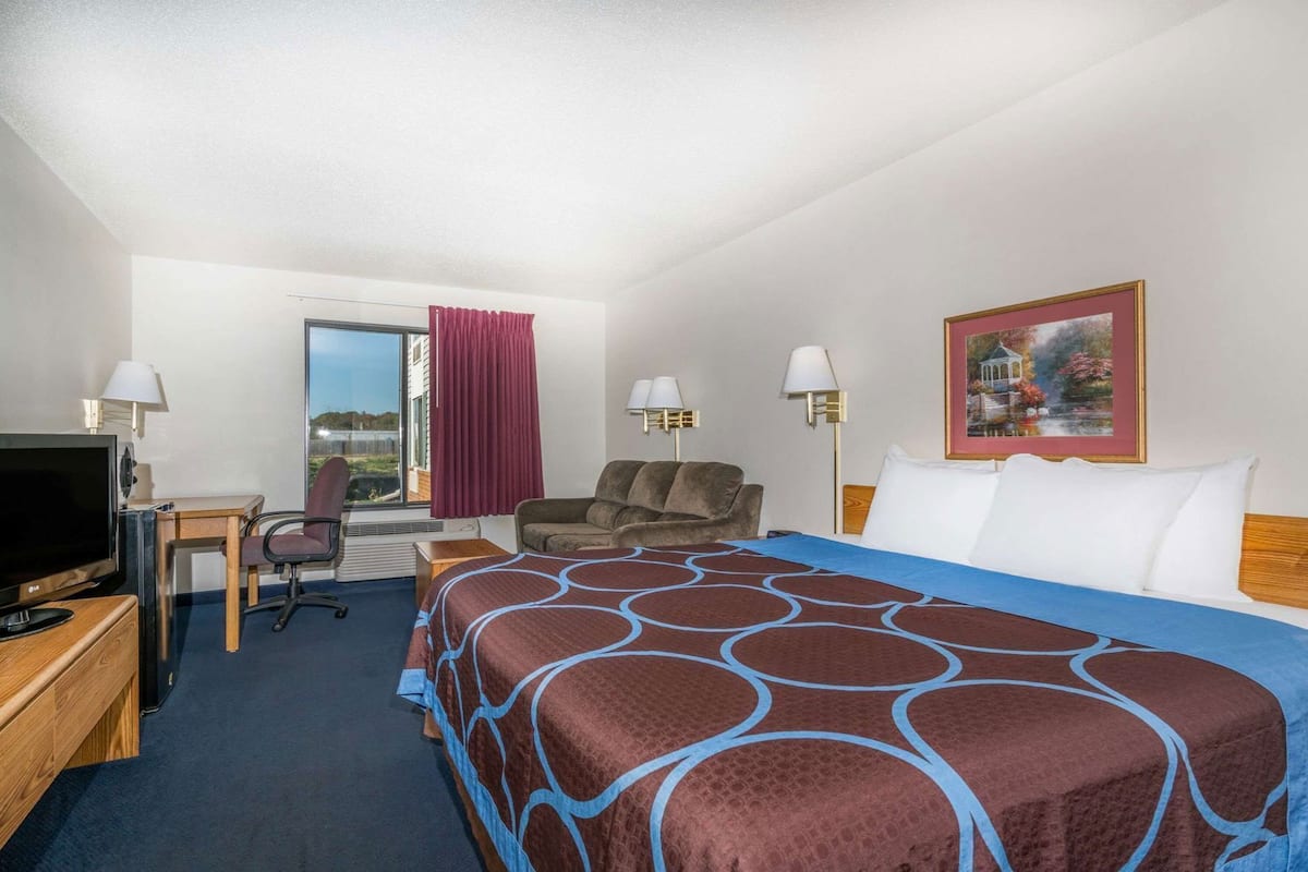 A hotel room with a bed, a desk with a TV, a chair, a couch, and a window with curtains.