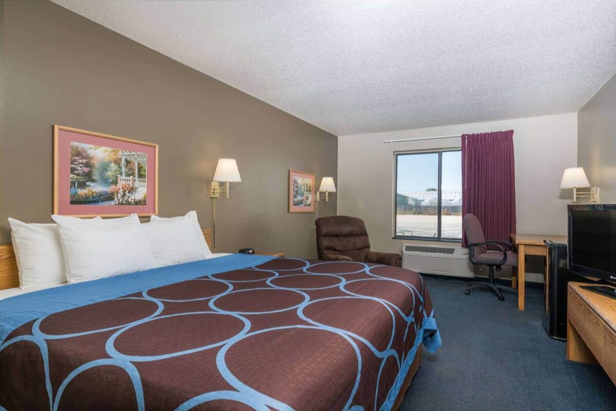 A hotel room with a large bed, two wall-mounted lamps, a desk with a TV, and a window with curtains.