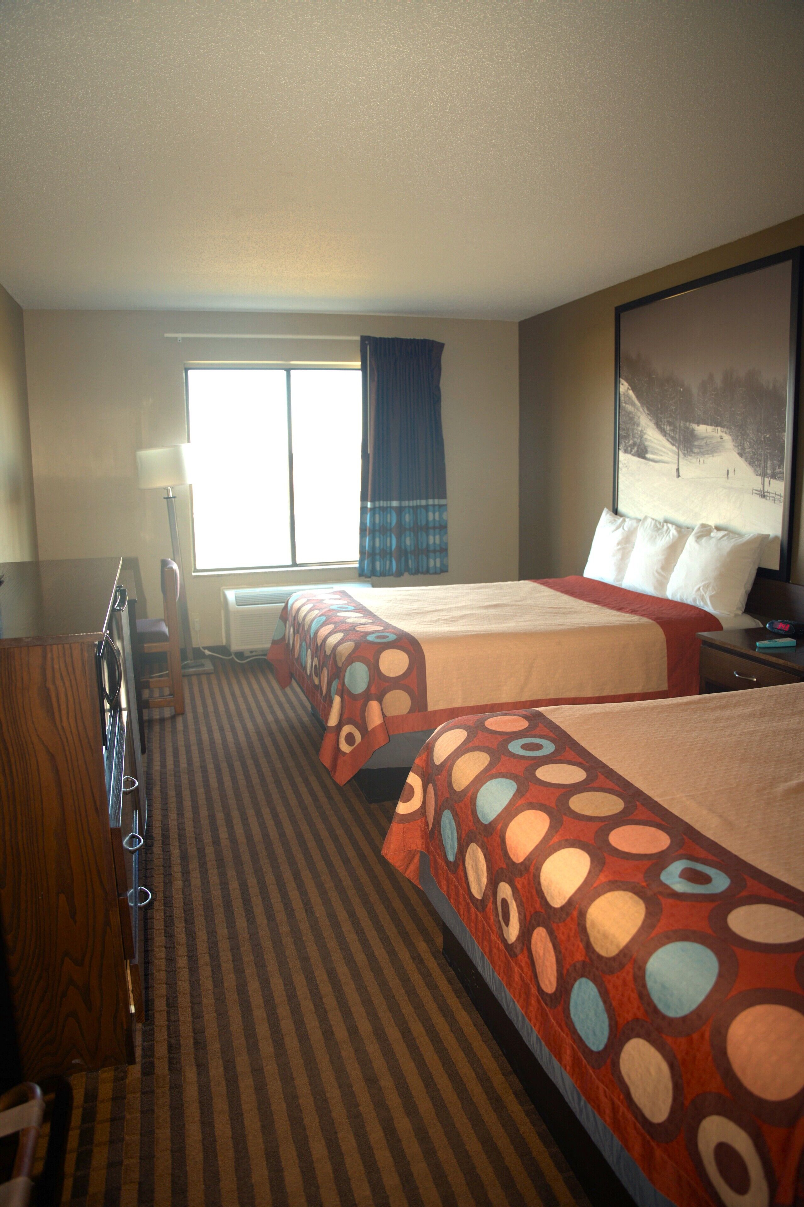 A hotel room with two beds, a desk, a chair, a lamp, and a large window with curtains.