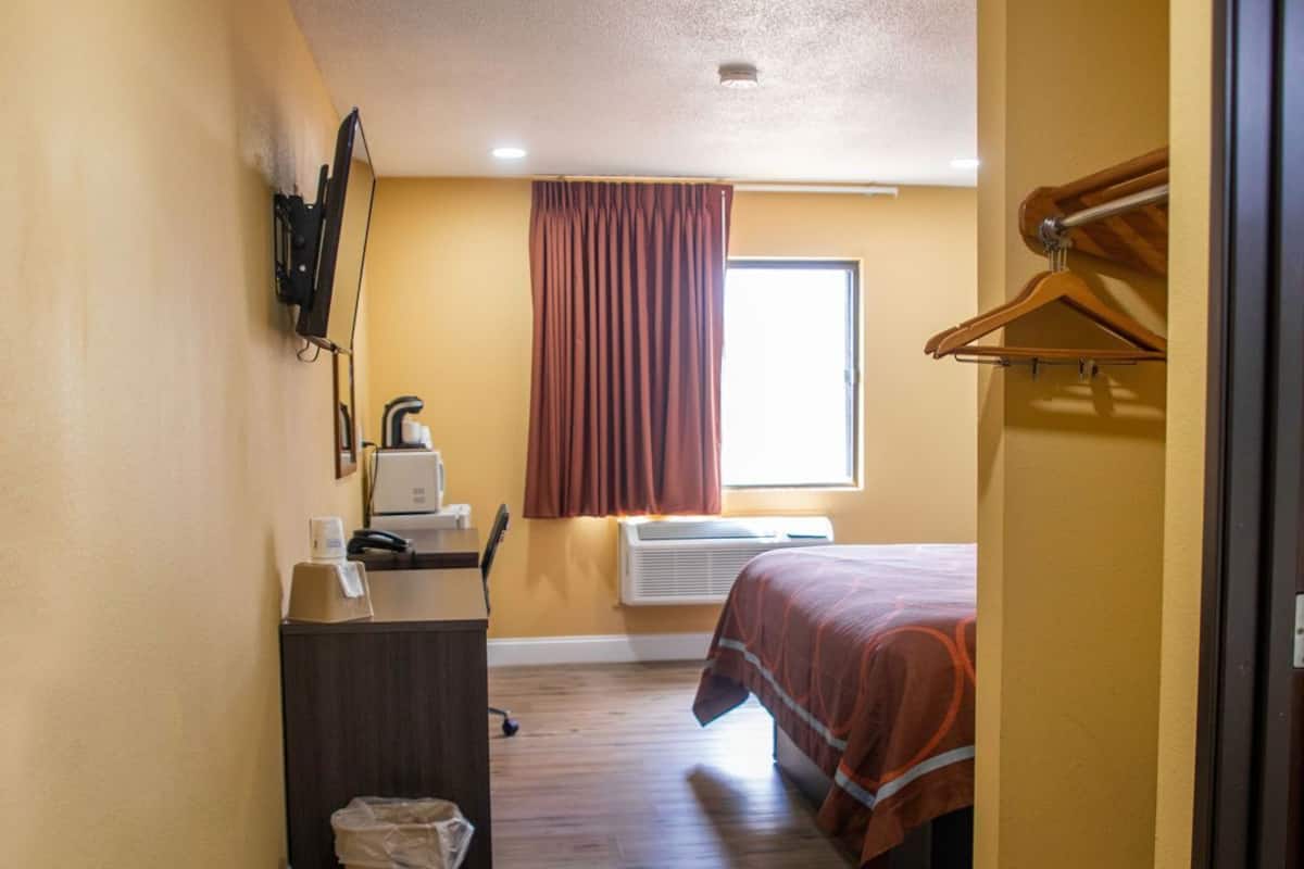 A narrow hallway with a bed, a desk, and a window with curtains.