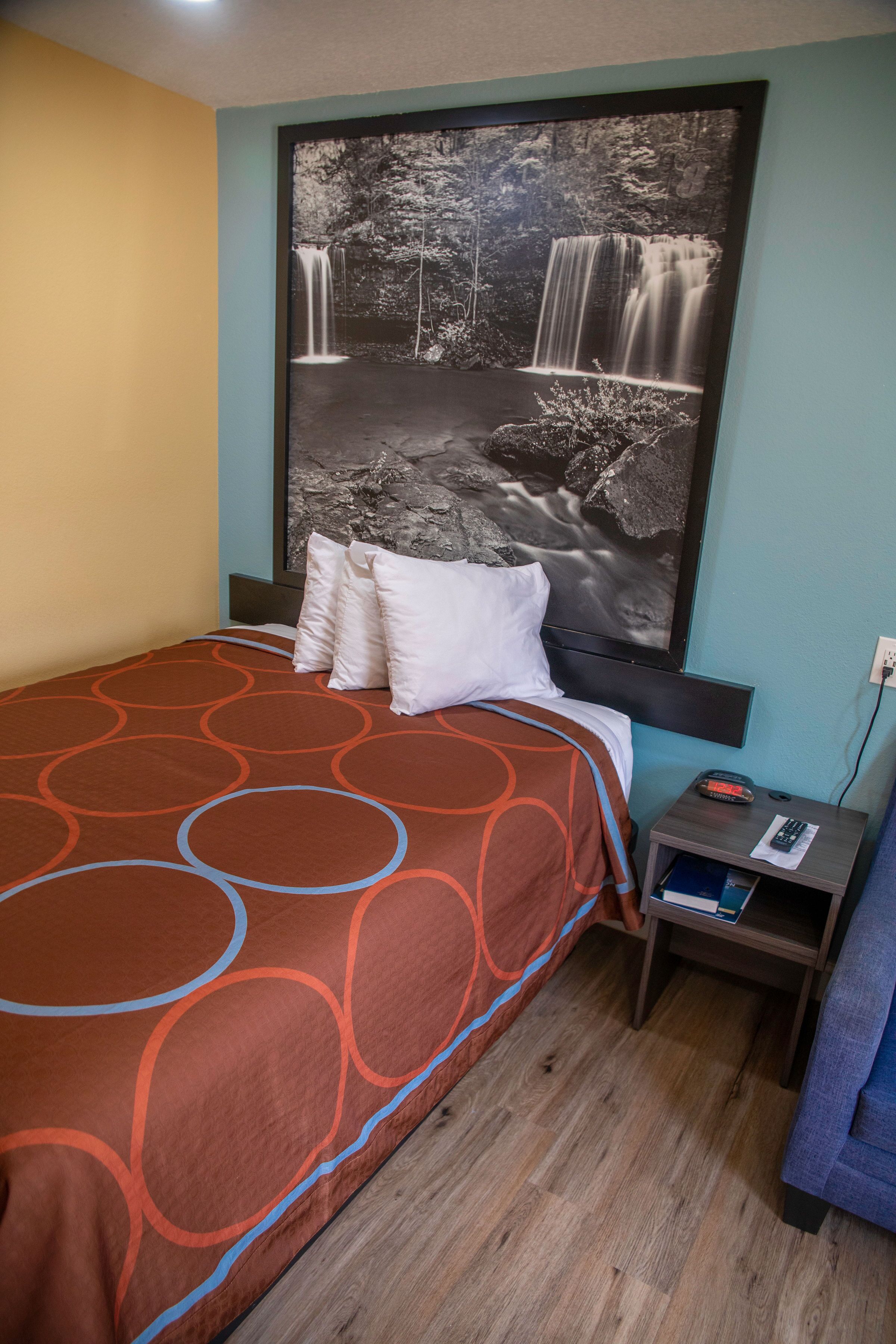 A hotel room with a bed, a nightstand, and a large wall mural of a waterfall.