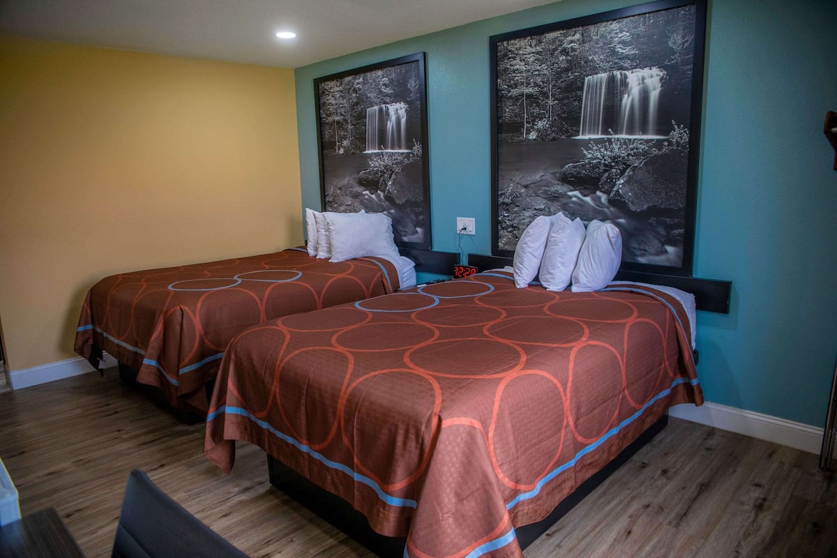 A hotel room with two beds, each with a patterned bedspread and white pillows. There are two large framed pictures of waterfalls on the wall.