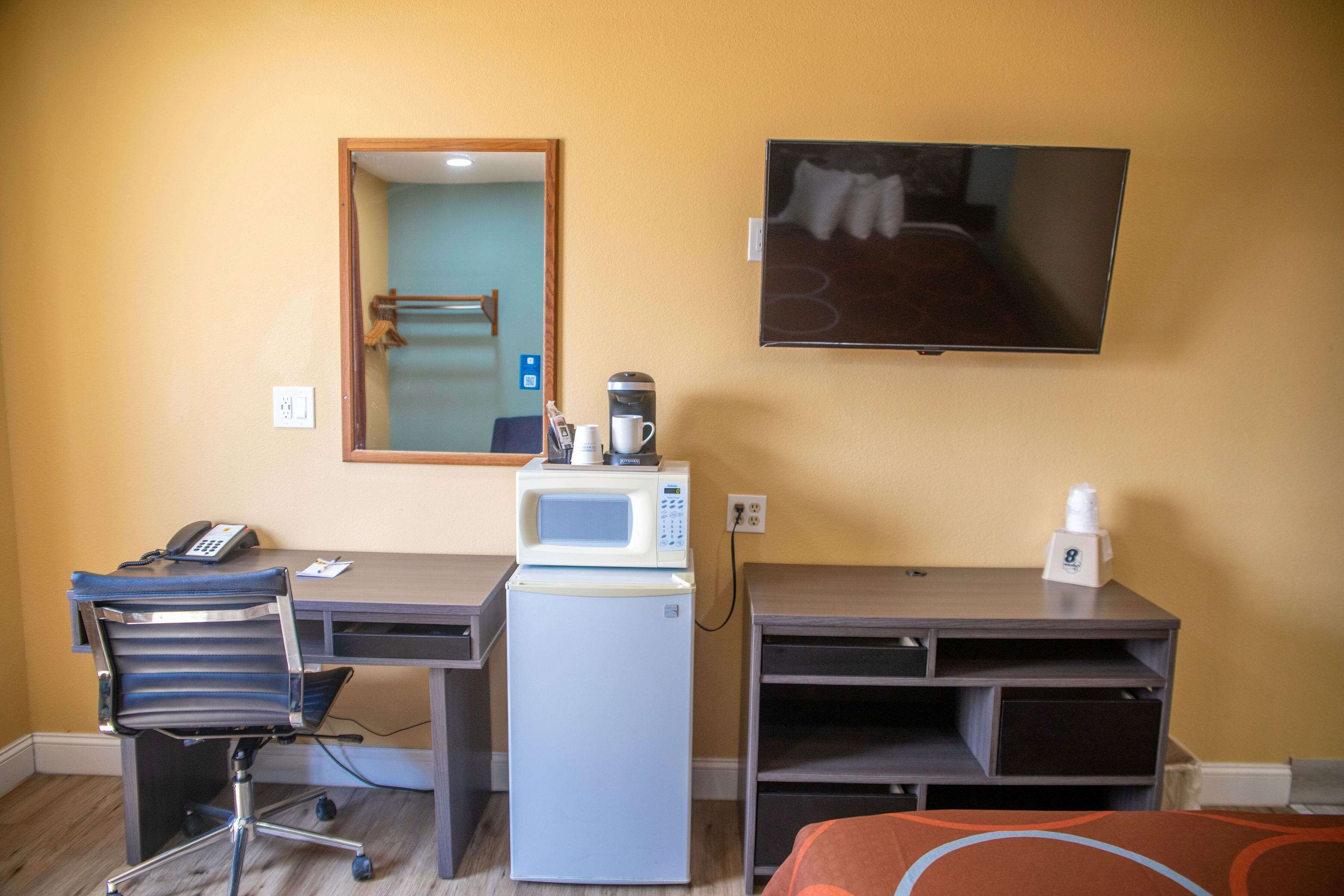 A hotel room with a desk, a microwave, a refrigerator, a chair, a TV, and a bed.