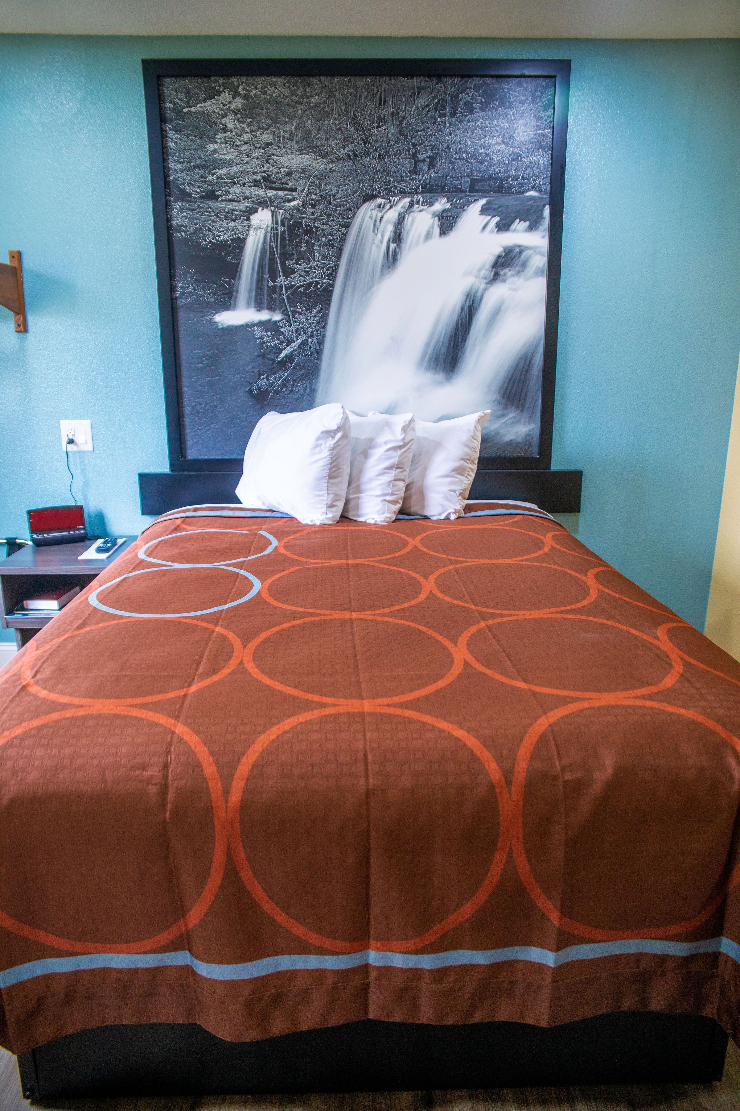 A hotel room with a bed, a nightstand, a TV, and a large framed picture of a waterfall.