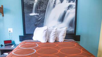 A hotel room with a bed, a nightstand, a TV, and a large framed picture of a waterfall.