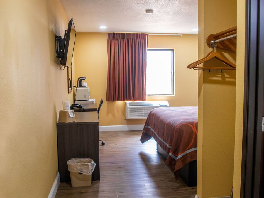 A narrow hallway with a desk, a bed, and a window with curtains.