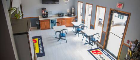 A hotel lobby with a reception desk, a coffee machine, and a seating area with tables and chairs.
