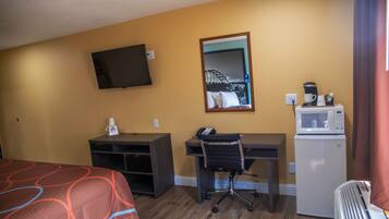 A hotel room with a bed, desk, chair, television, and a refrigerator.